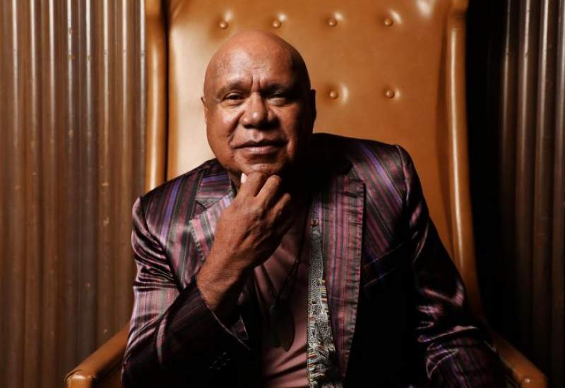 Archie Roach sits on a leather chair